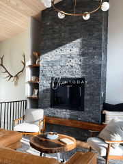 living room with brown leather cough and two white chairs with wood circle coffee table. Gas fireplace in a gray stone surround that goes up the wall, deer antlers on the left