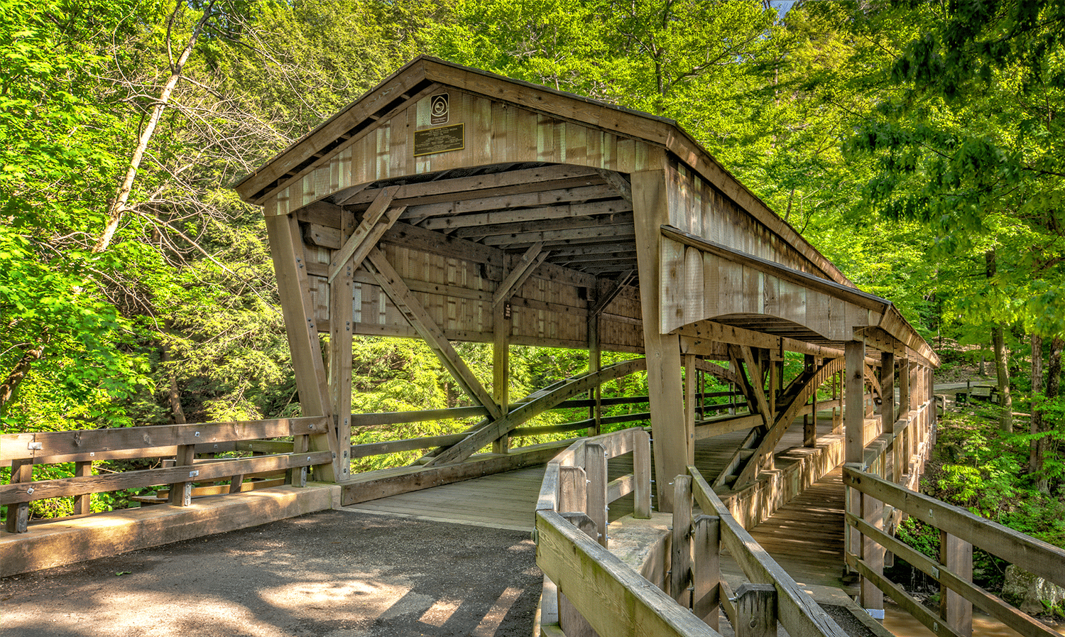 horizontal photo of the covered bridge at Lanterman's Mill. A wooden bridge with a lot of green trees around it. Image via Canva pro license