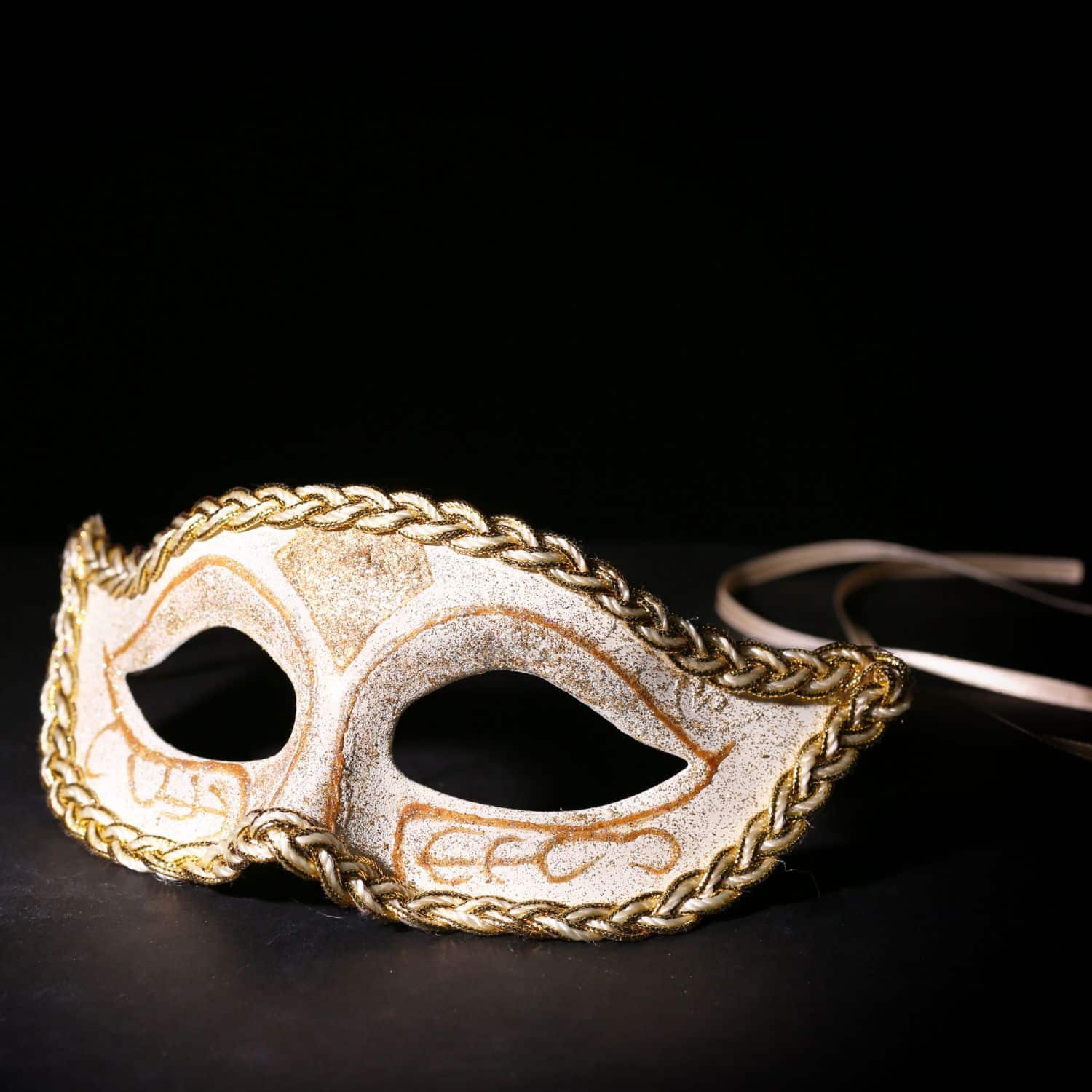 A cream & gold colored masquerade mask ona black background