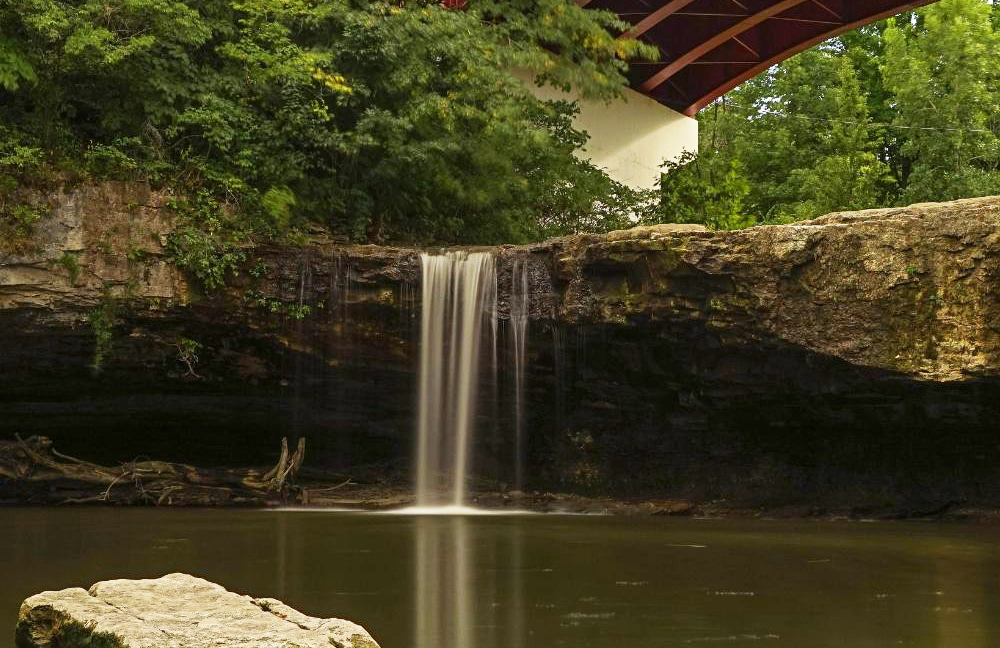 A photo of a waterfall underneath a red bridge. This photo is from Ludlow Falls