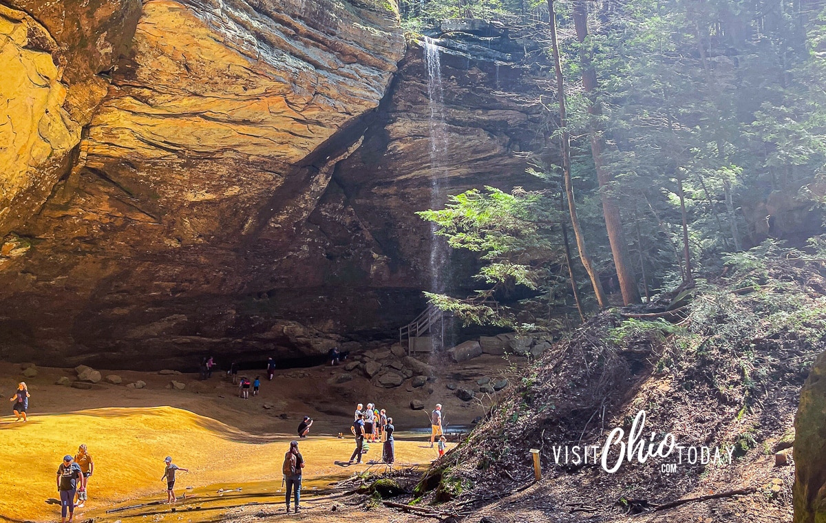 A photo of the waterfall in Ash Cave, Hocking Hills State Park. There are people at the bottom, admiring the view. Photo credit: Cindy Gordon of VisitOhioToday.com