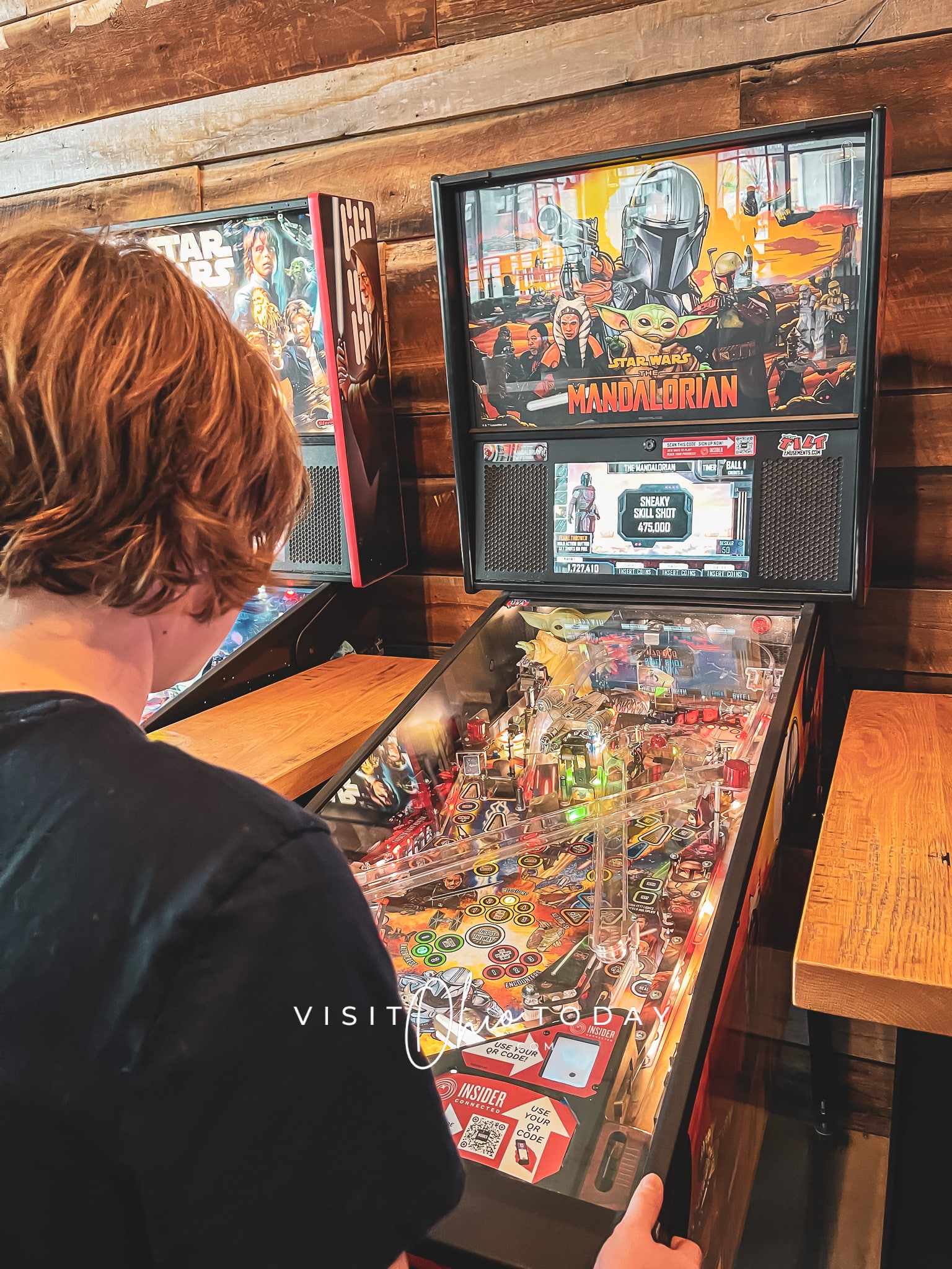 IMAGE  of boy playing a pinball machine that is lighting up