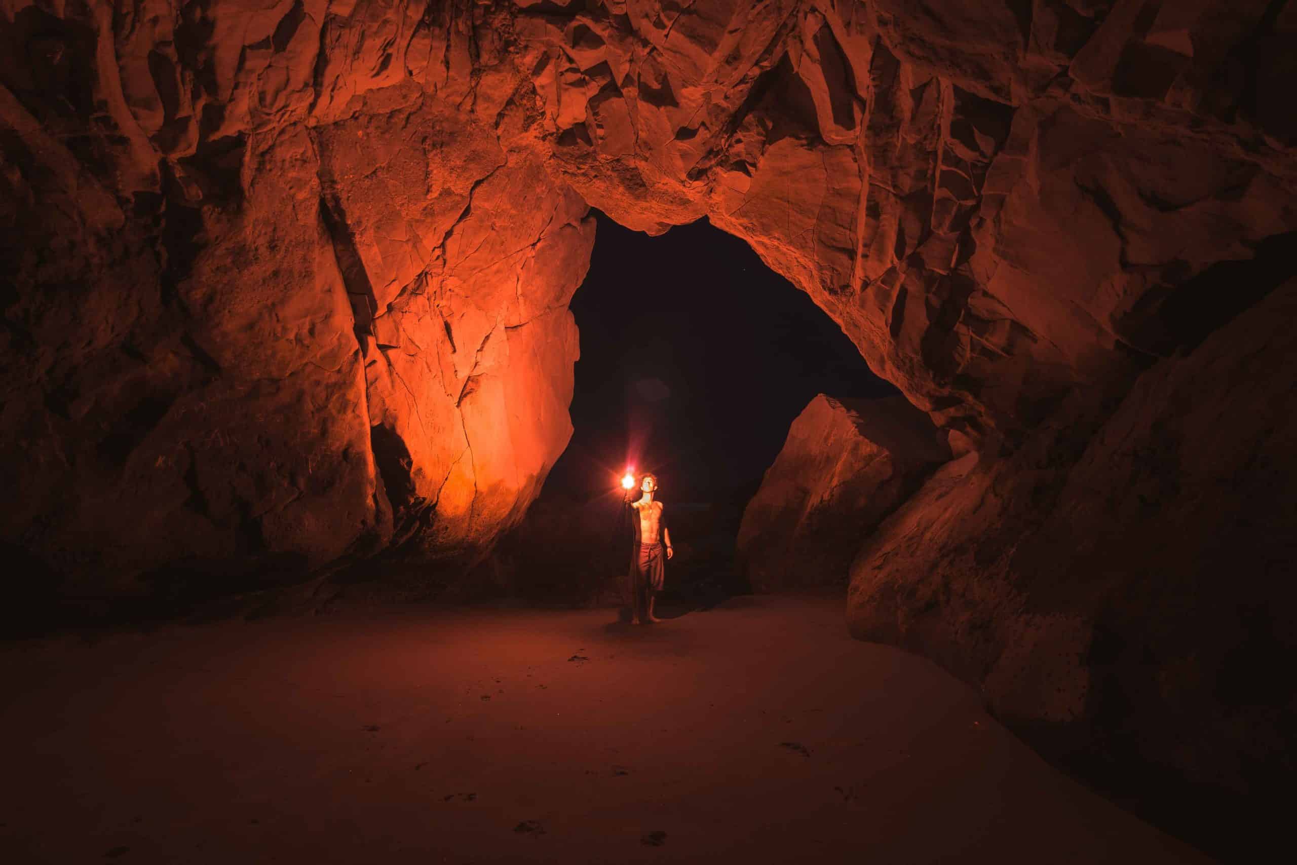 A figure walking through a cave using a flashlight