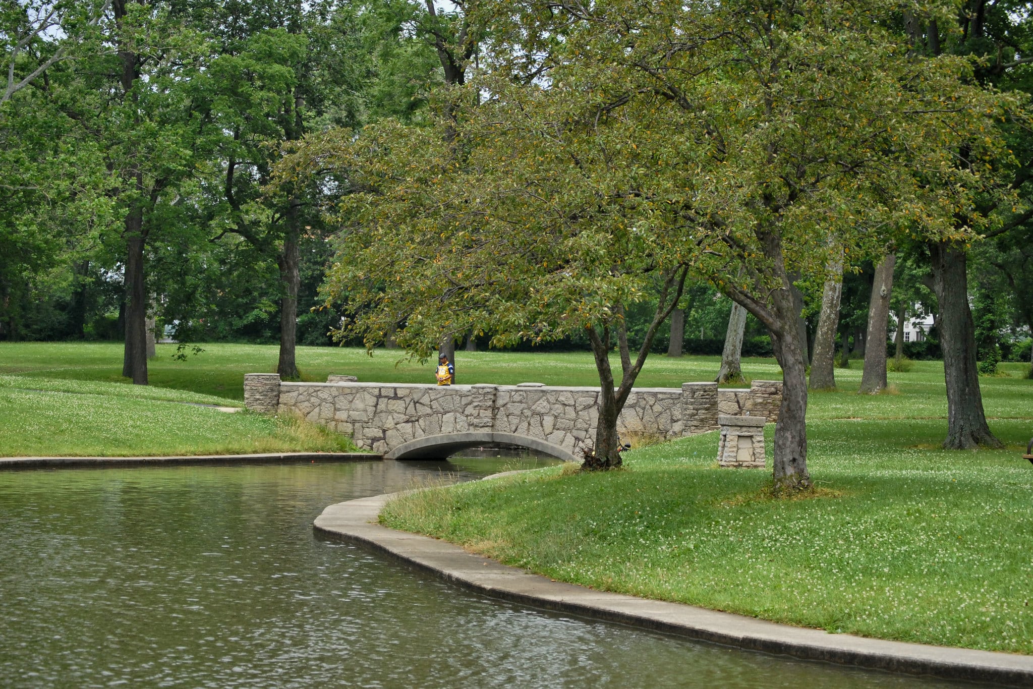 horizontal photo showing a bridge over a river at faurot park, lima ohio, with grass and trees either side of the river