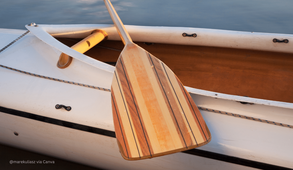 horizontal close-up photo of a white canoe with a paddle laying across it