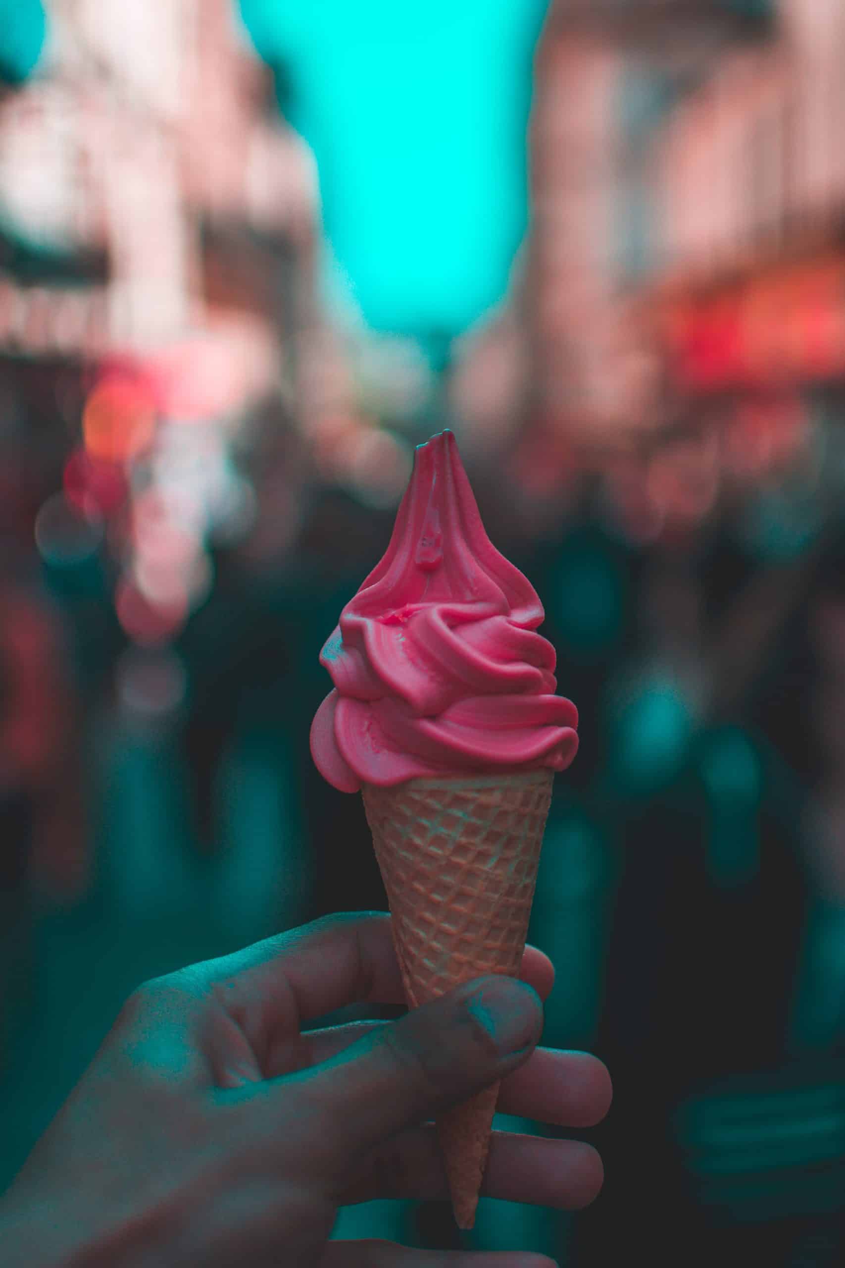 A hand holding a bright pink coloured ice cream against a blurred city background