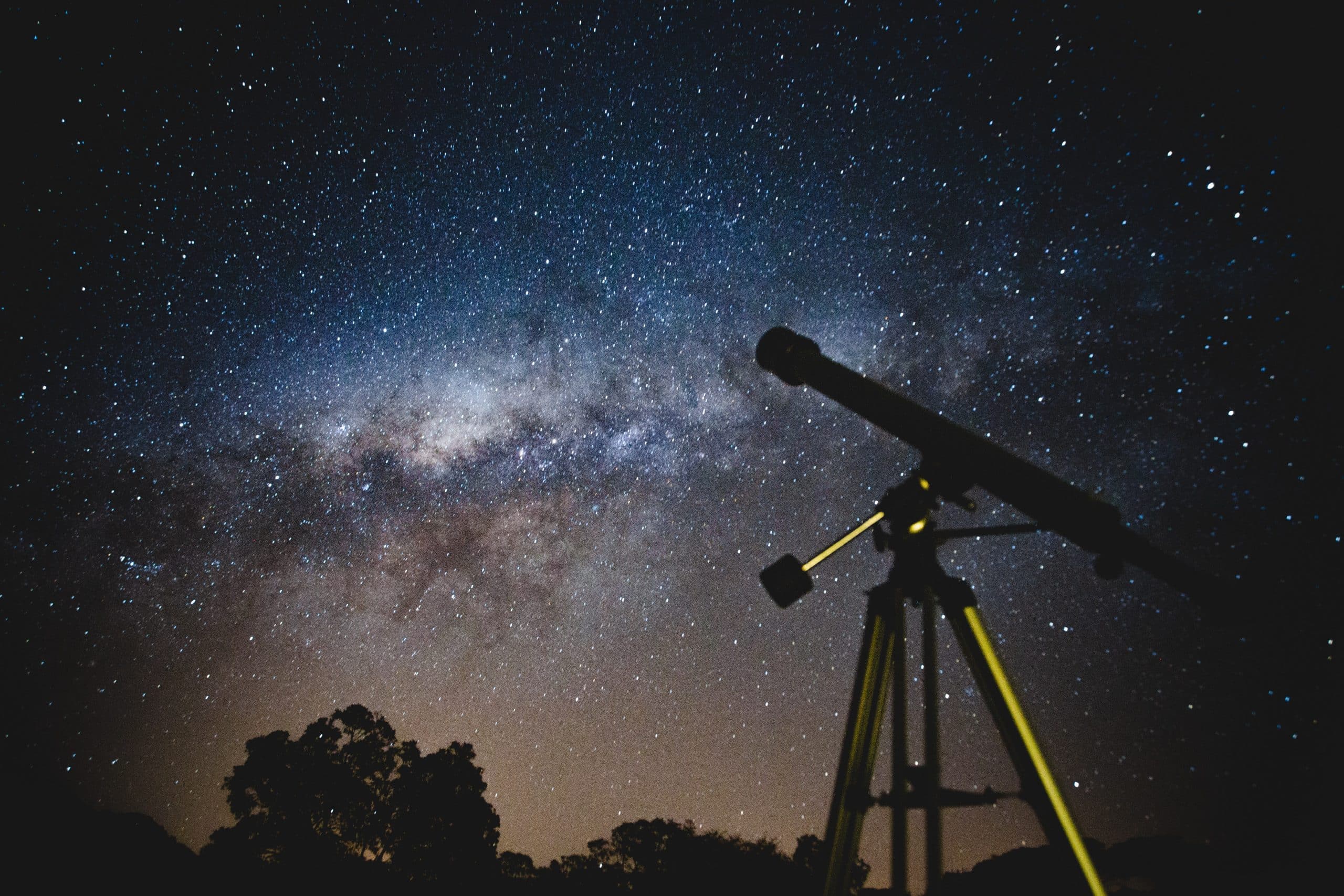 A night sky filled with stars. A telescope is set up underneath