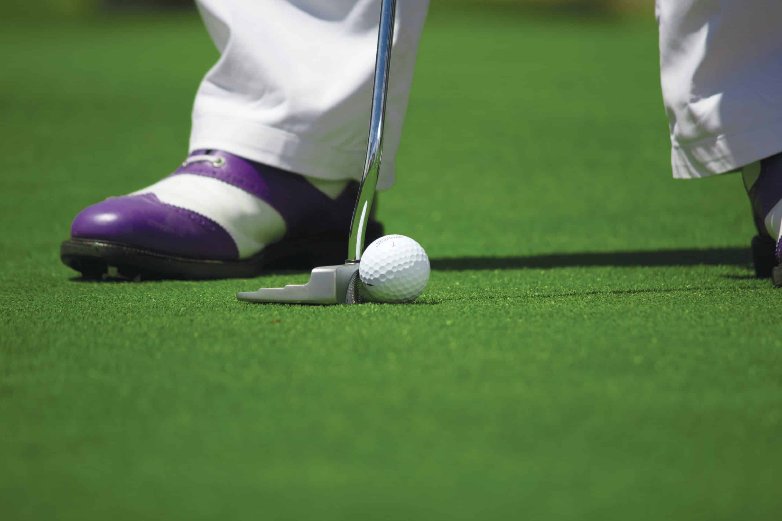 Someone playing golf, with only their feet, golf club and golf ball visible 