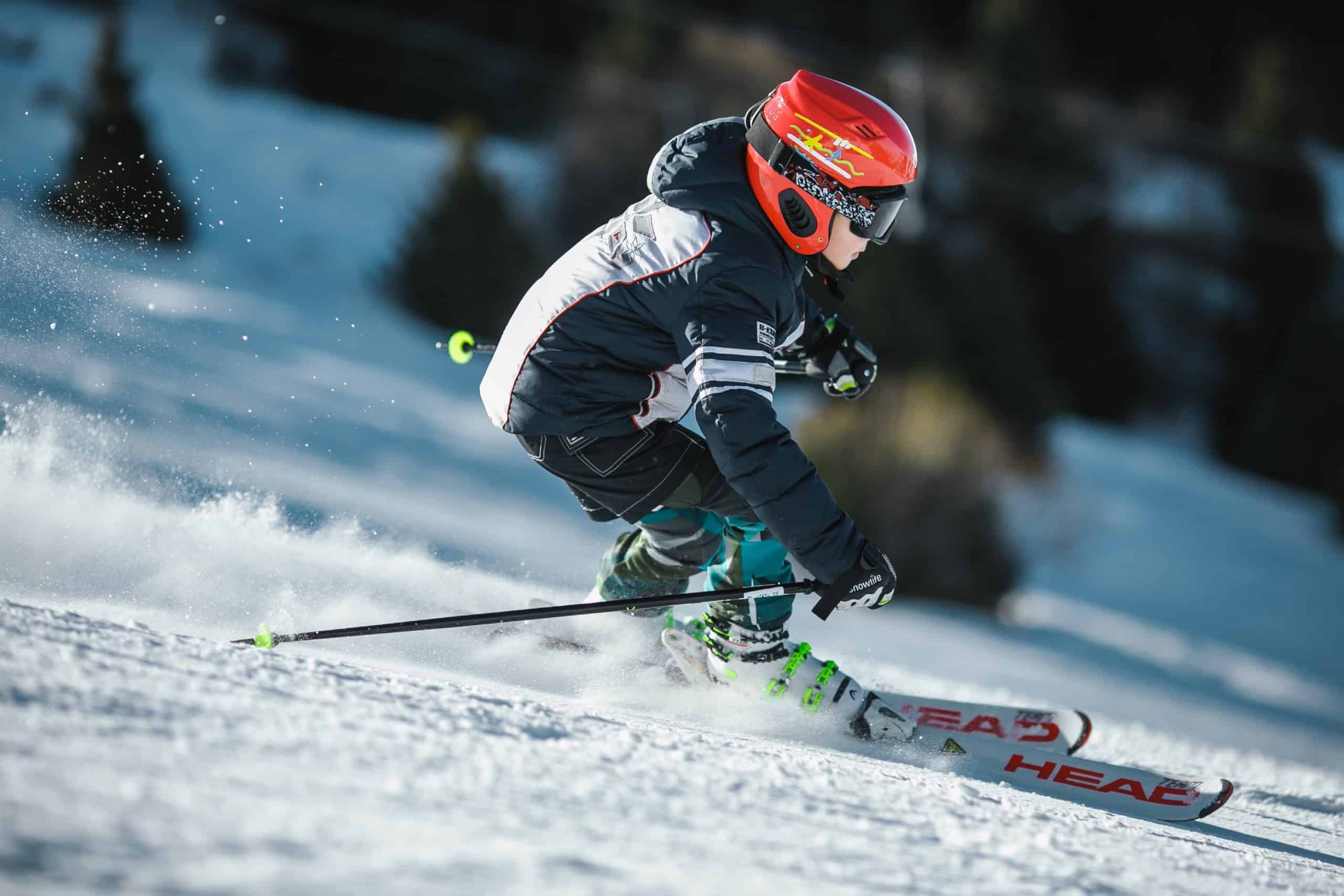 A child wearing a red helmet and black goggles skiing