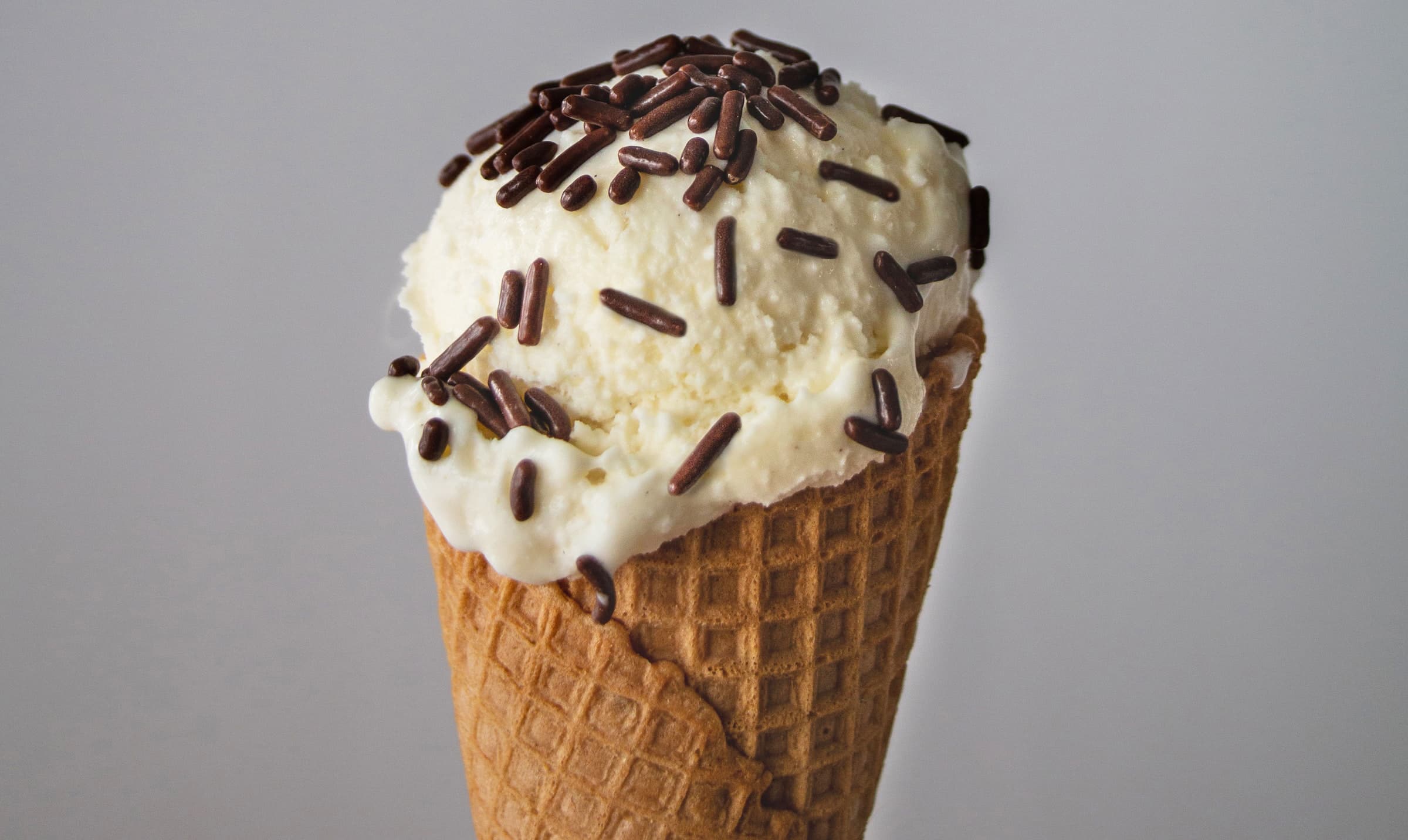 horizontal photo of an ice cream cone with vanilla ice cream and chocolate sprinkles