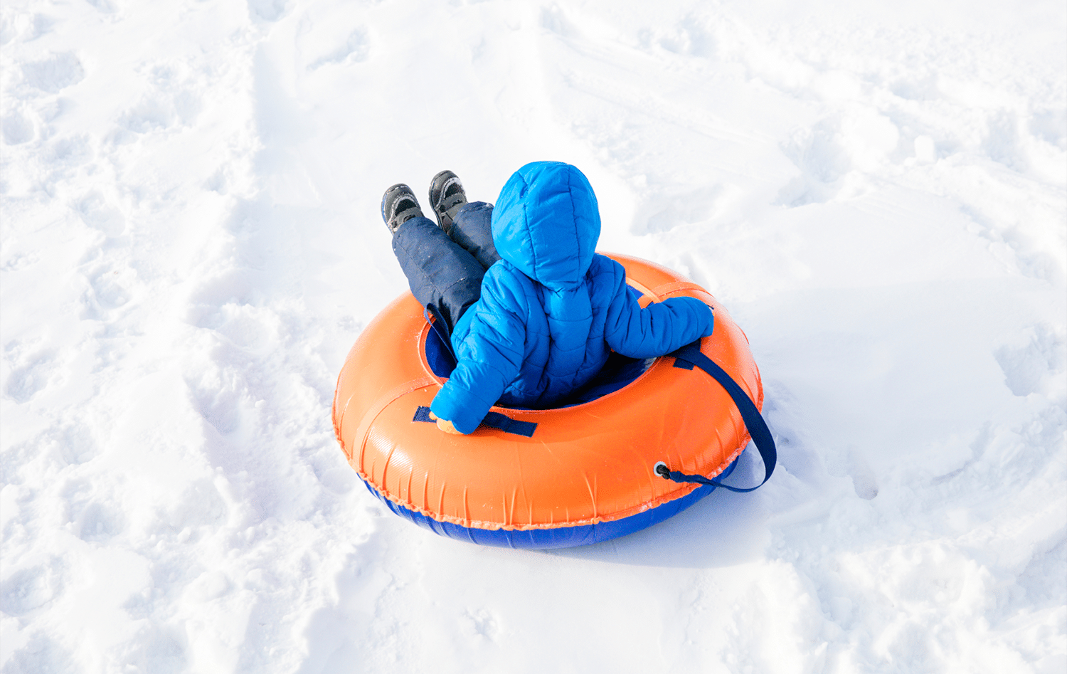 horizontal photo of a small child snow tubing on an orange tube
