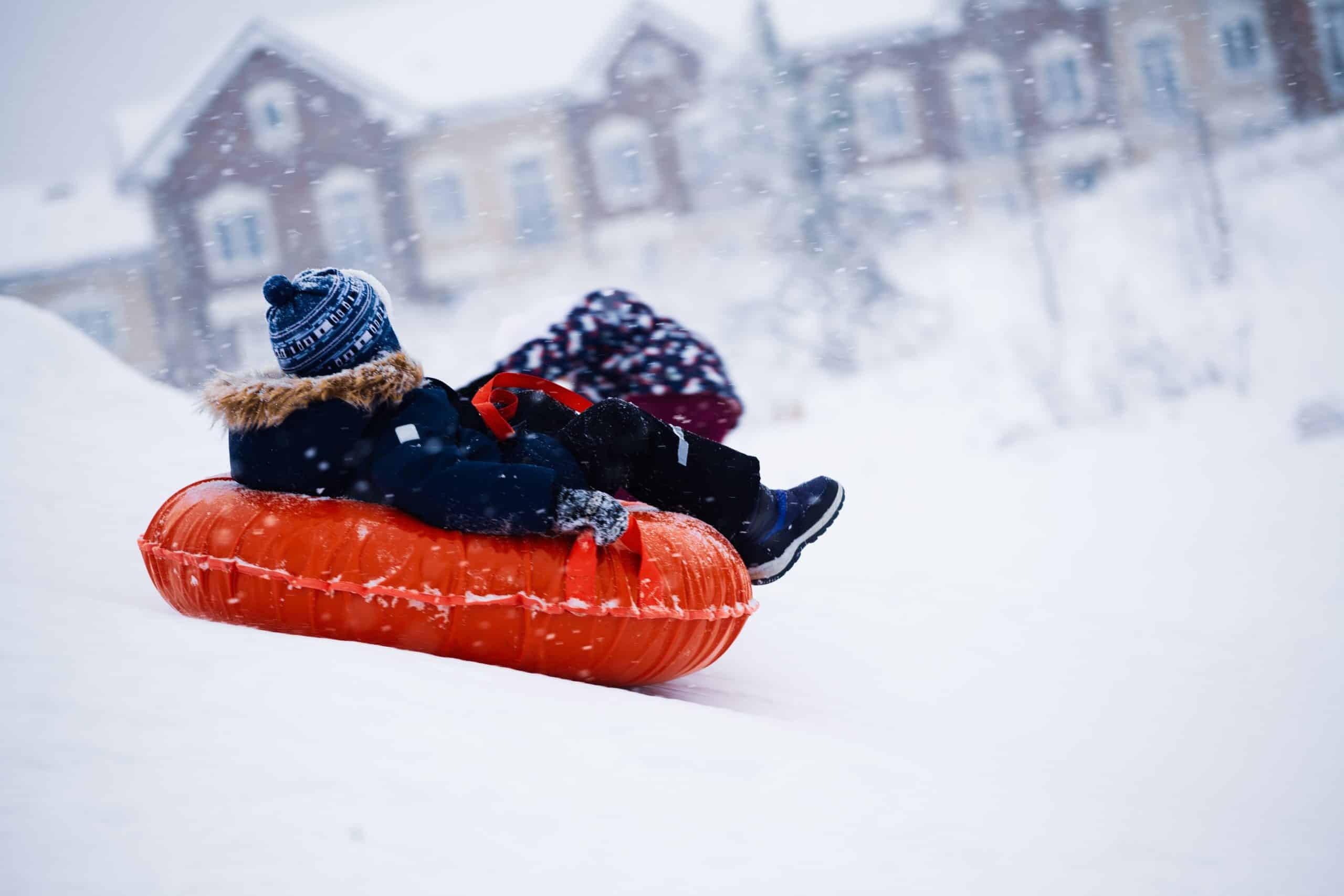 A youth sliding down a snowy hill on a red rubber tyre