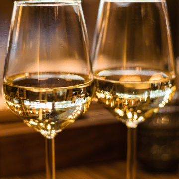 A close up photo of two wine glasses each containing white wine