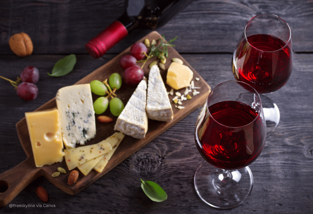 horizontal photo of two glasses of wine and a cheese board on a dark gray surface