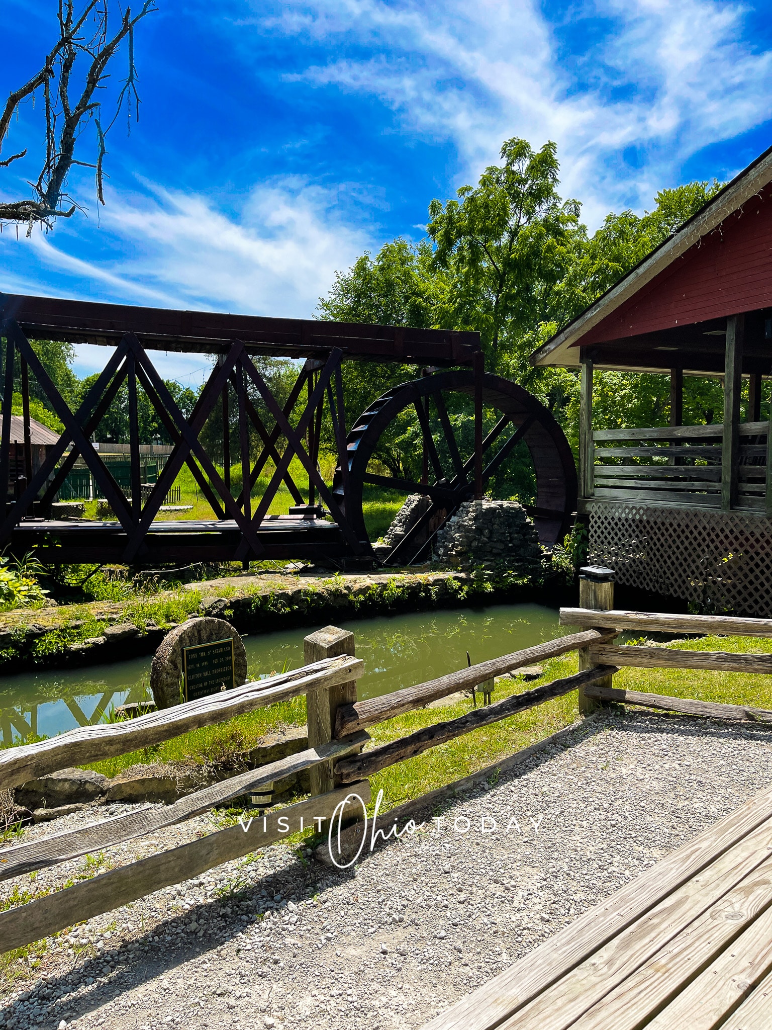 vertical photo of clifton mill showing the mill wheel and the little miami river along with the footbridge
