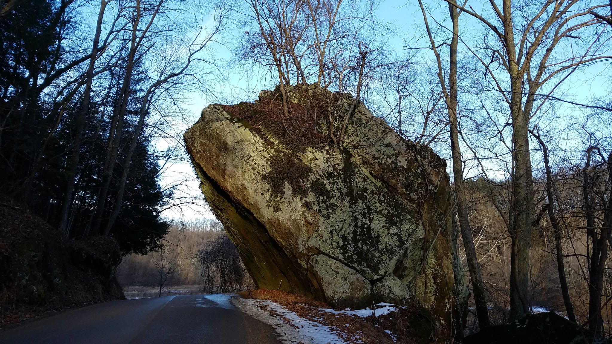 horizontal photo of a large rock overhanging the road at clear creek metro park. Trees and foliage line the road in this winter shot