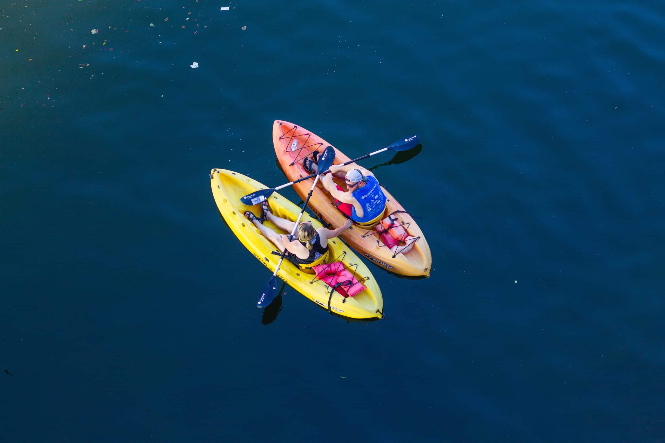 horizontal photo of an overhead shot of 2 kayaks with a man and a woman in them on deep blue water