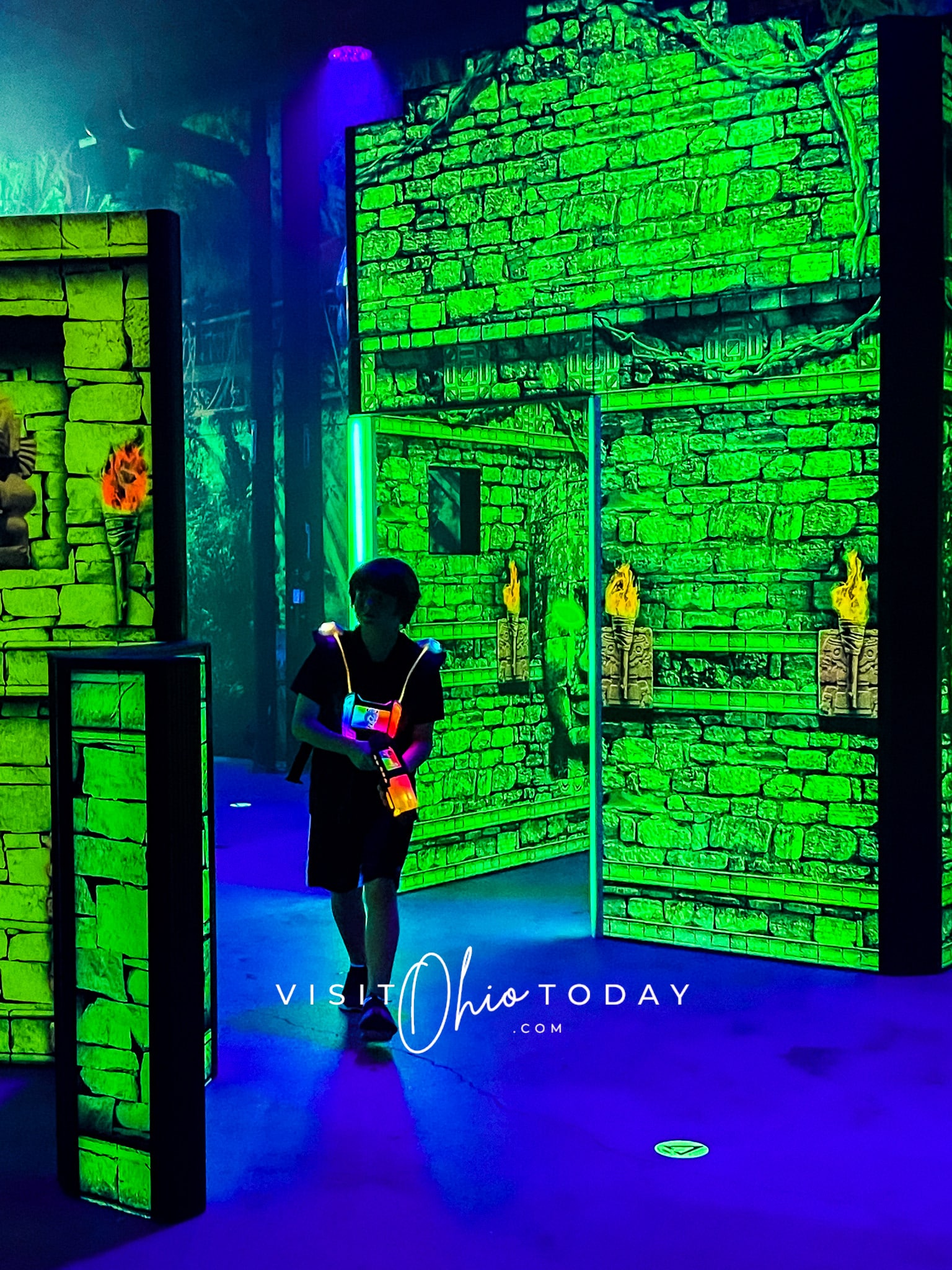 vertical photo of a boy playing Laser Tag at Scene75 Columbus, surrounded by green and blue lights
