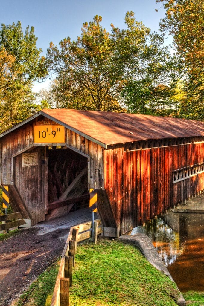 vertical photo of Benetka Road Covered Bridge with trees in the background and road and grass in the foreground