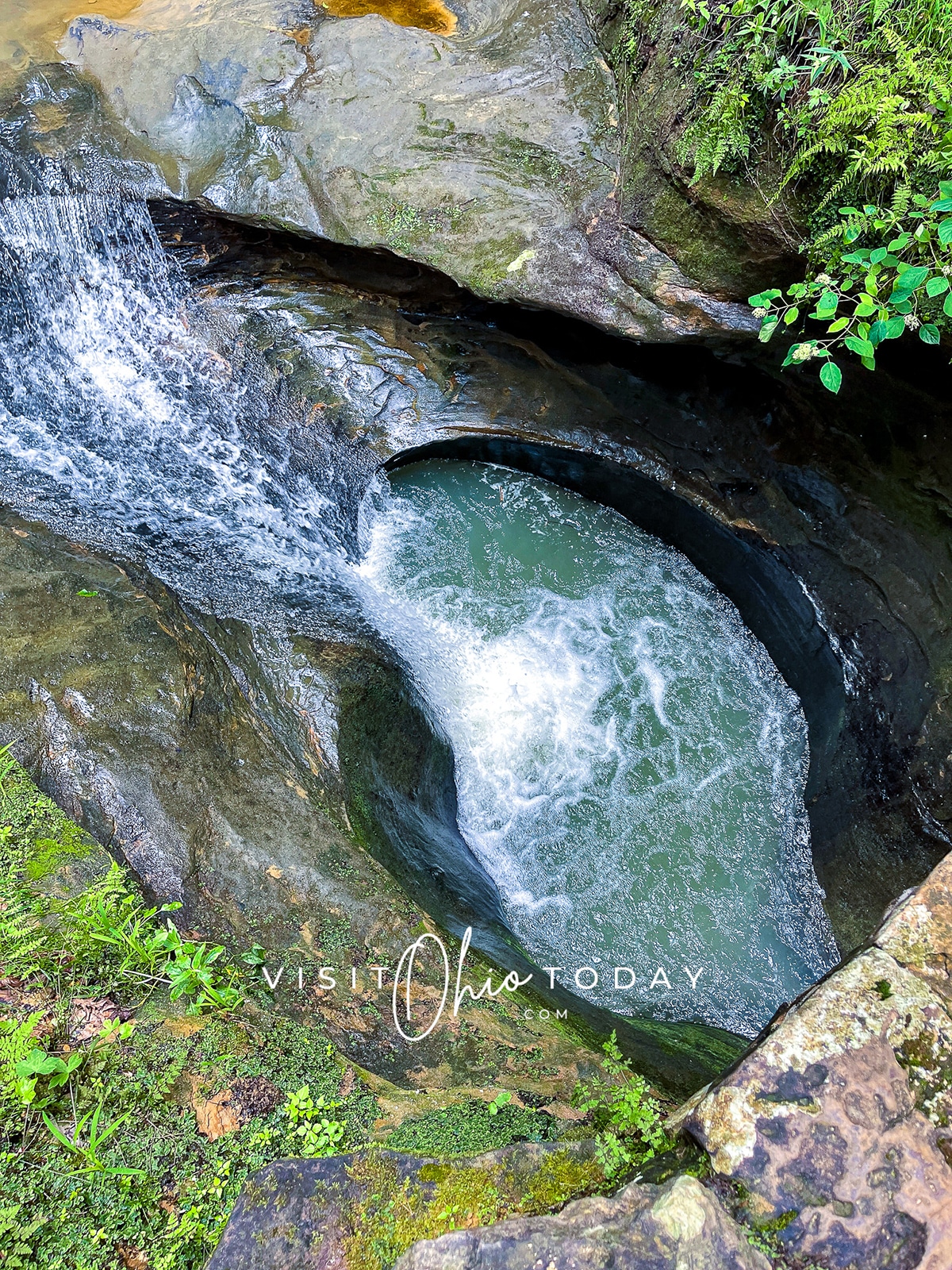 vertical photo that is an overhead shot of Devils Bathtub Hocking Hills. It shows the waterfall falling into the pool