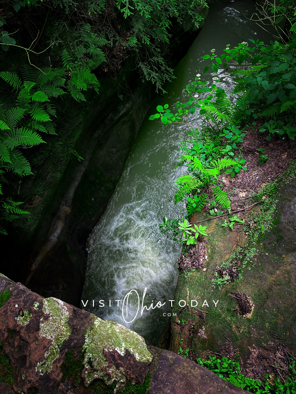 horizontal photo showing the water running from Devils Bathtub Hocking Hills with foliage on both banks