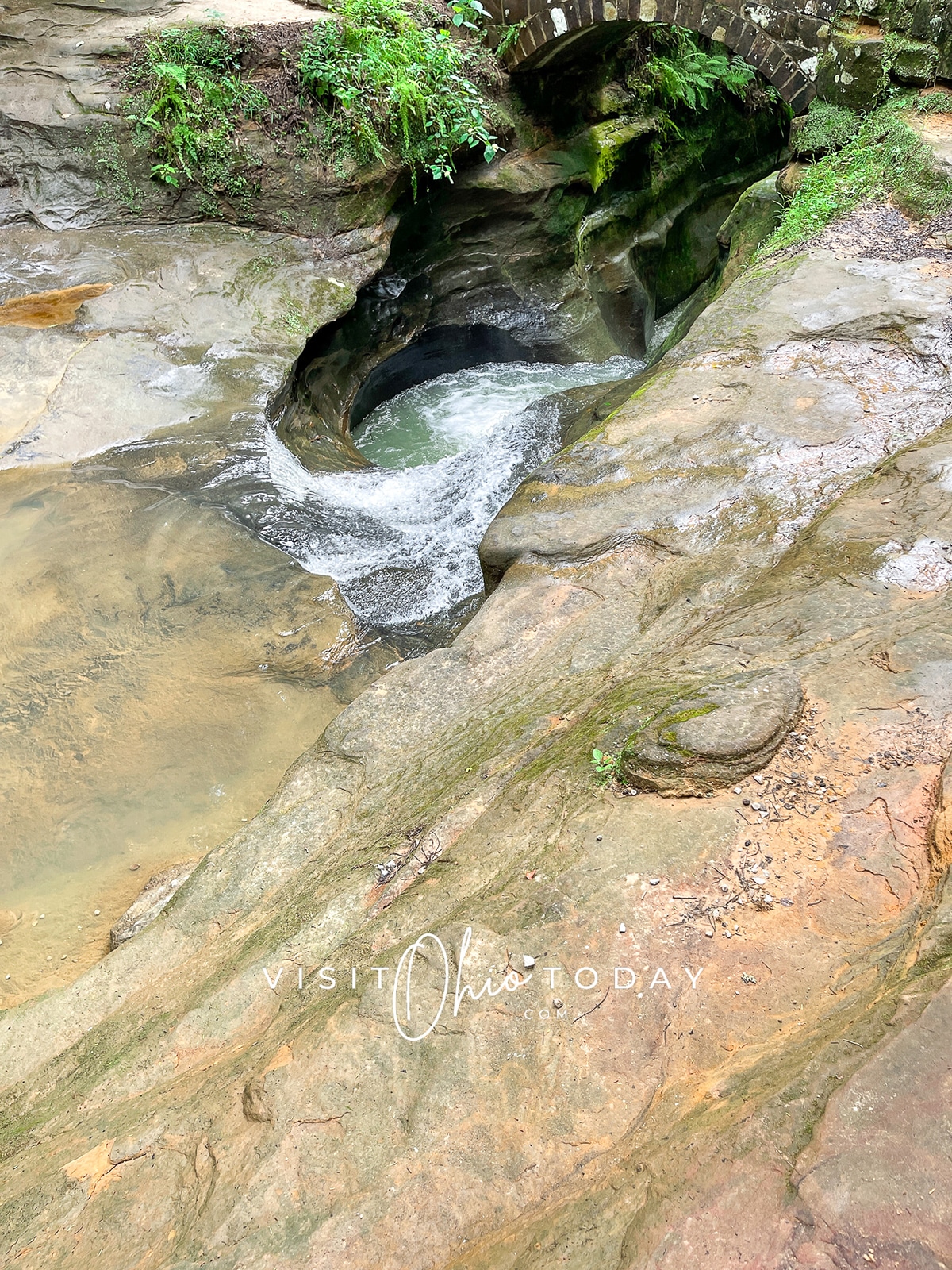 vertical photo of Devils Bathtub Hocking Hills showing the water swirling into the pool