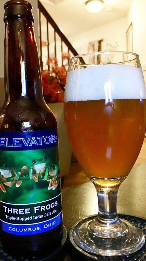 vertical photo showing a bottle of elevator three frogs triple hoped India pale ale with a glass of beer beside it