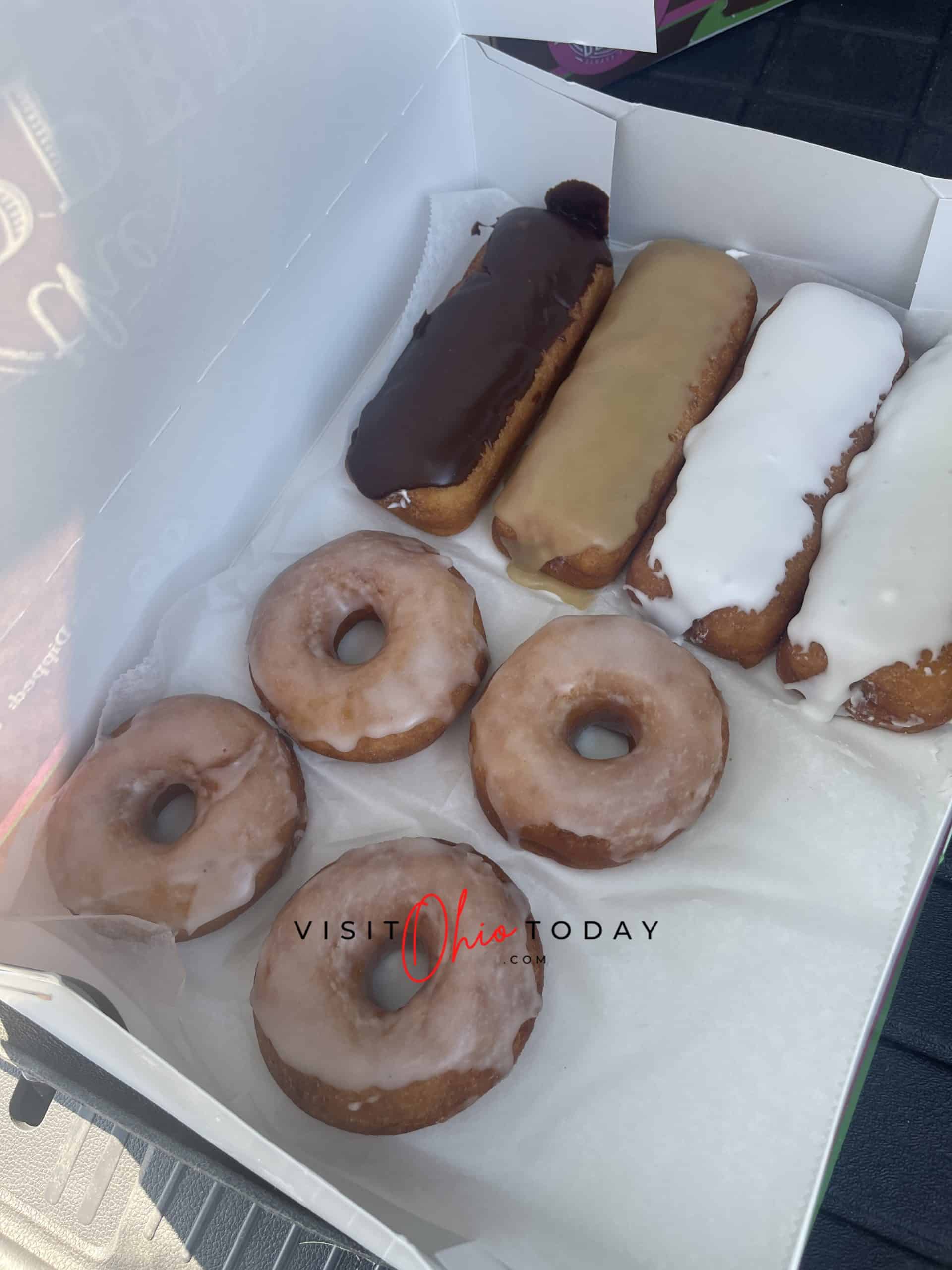 vertical photo showing a box of donuts from gluten free from the dipped. 4 round donuts and 4 finger donuts