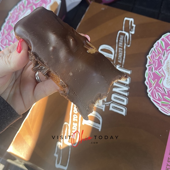 square photo showing a hand holding a chocolate covered gluten free long donut