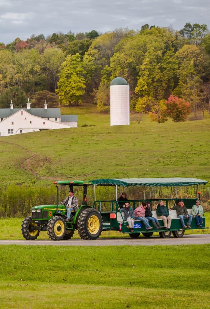 vertical photo of a tractor ride at heritage days festival with green fields and a farm in the background