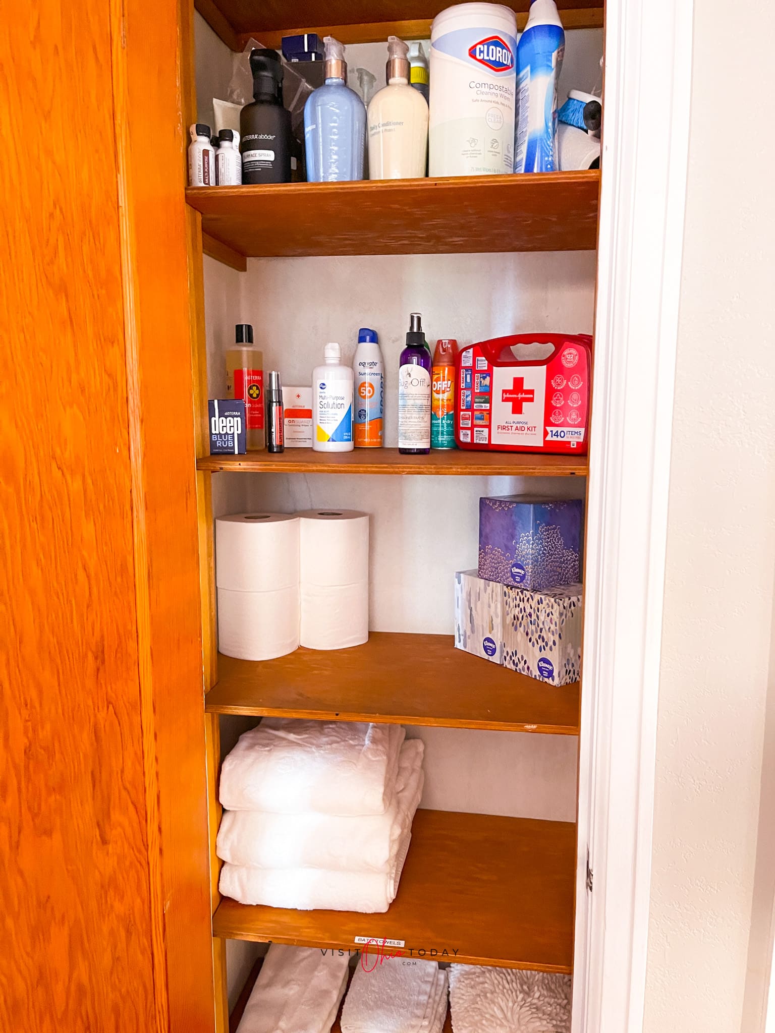 hallway closet that is open, it has a wooden door and wooden shelves. On shelves are neatly packed/stacked towels, toilet paper and first aid and toiletry products Photo credit: Cindy Gordon of VisitOhioToday.com