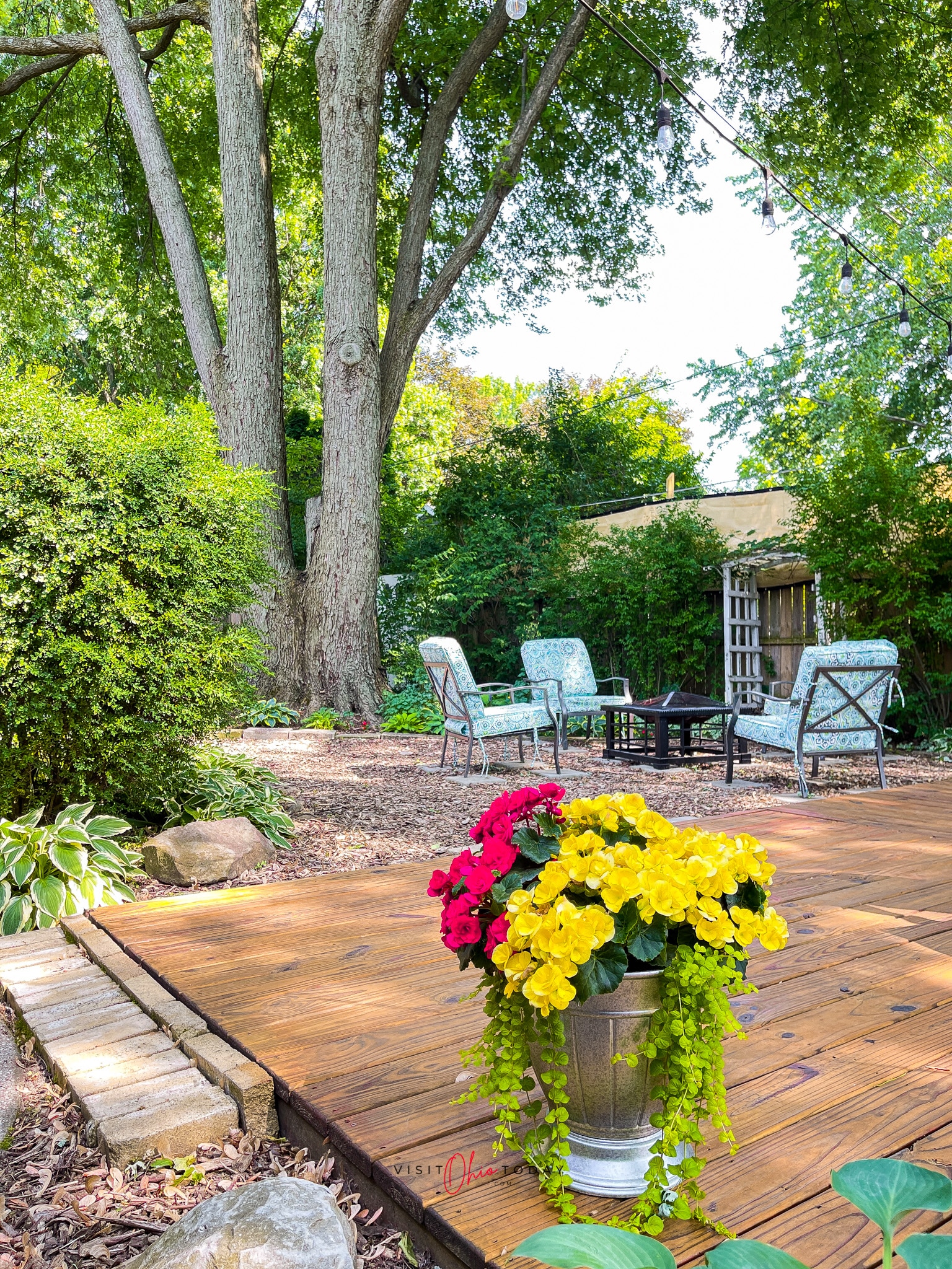 backyard oasis, wooden deck with colorful potted flowers and mulched fire pit area with four chairs