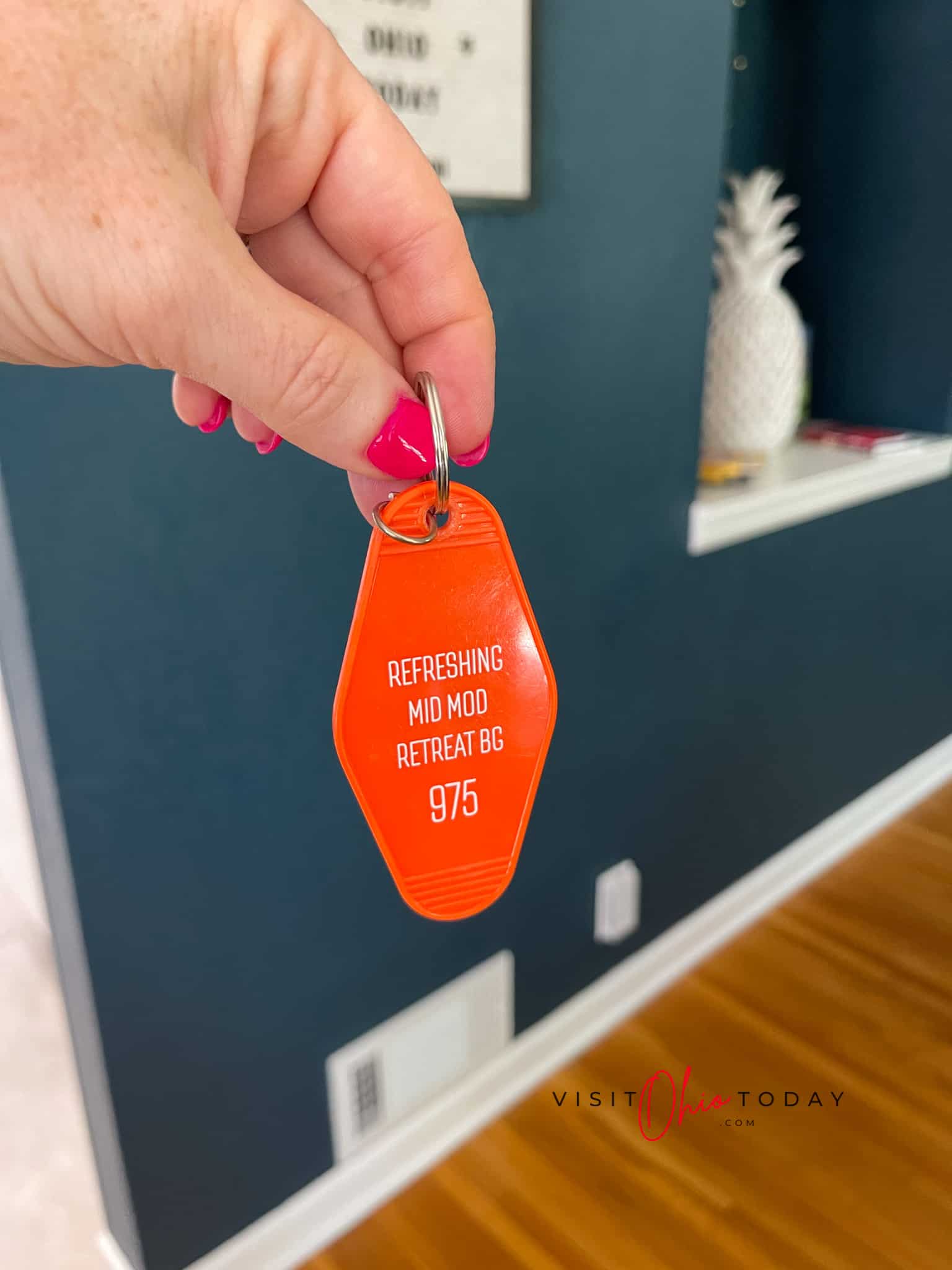 blue walls, fingers with neon pink nails holding an orange keychain that says "freshing mid mod retreat bg " Photo credit: Cindy Gordon of VisitOhioToday.com