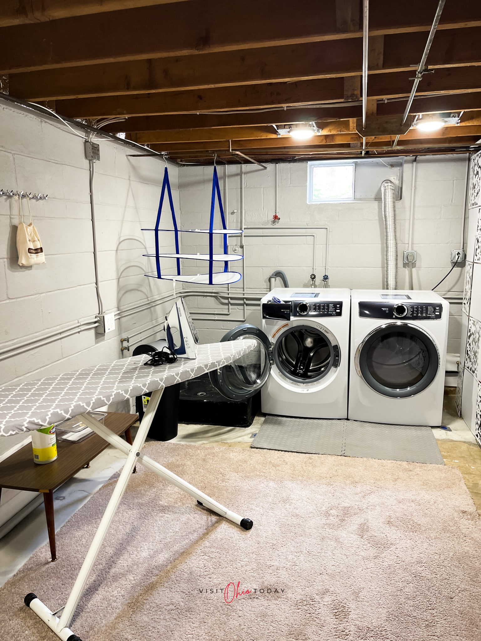 basement room with carpet, white washer and dryer and ironing board