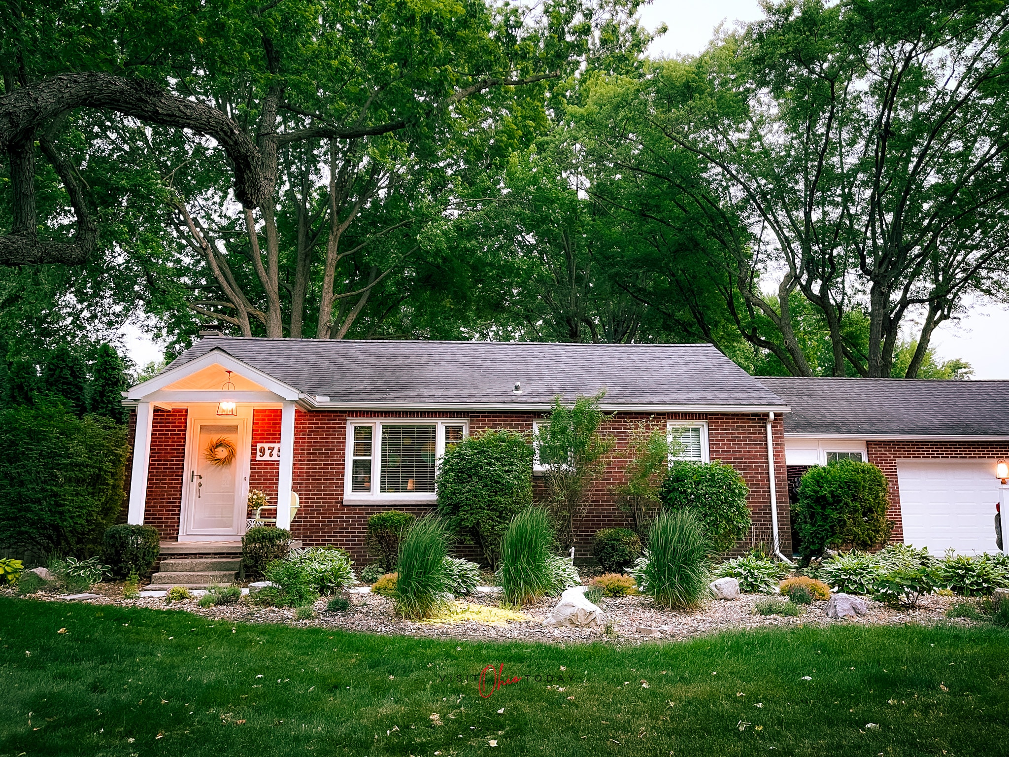 brick house in bowling green ohio with lots of green trees and green grass and green plants around it, the porch light is on Photo credit: Cindy Gordon of VisitOhioToday.com