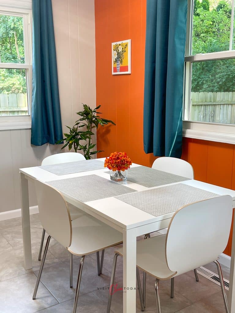 white kitchen table and chairs, orange painted walls, blue curtains on windows