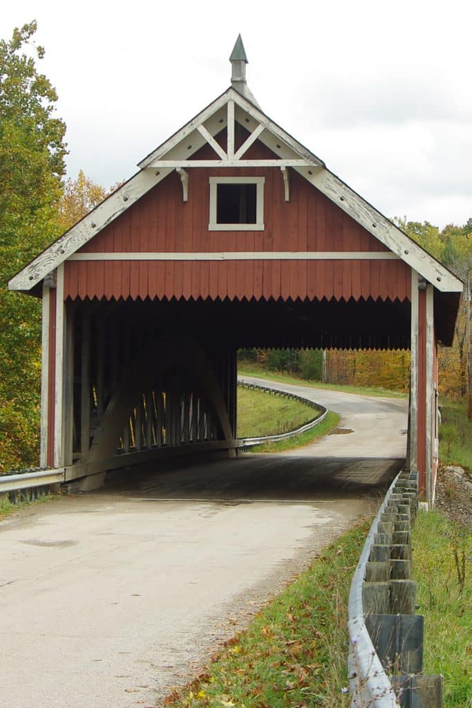 vertical photo of the netcher road covered bridge showing the road going through the bridge and countryside around the bridge