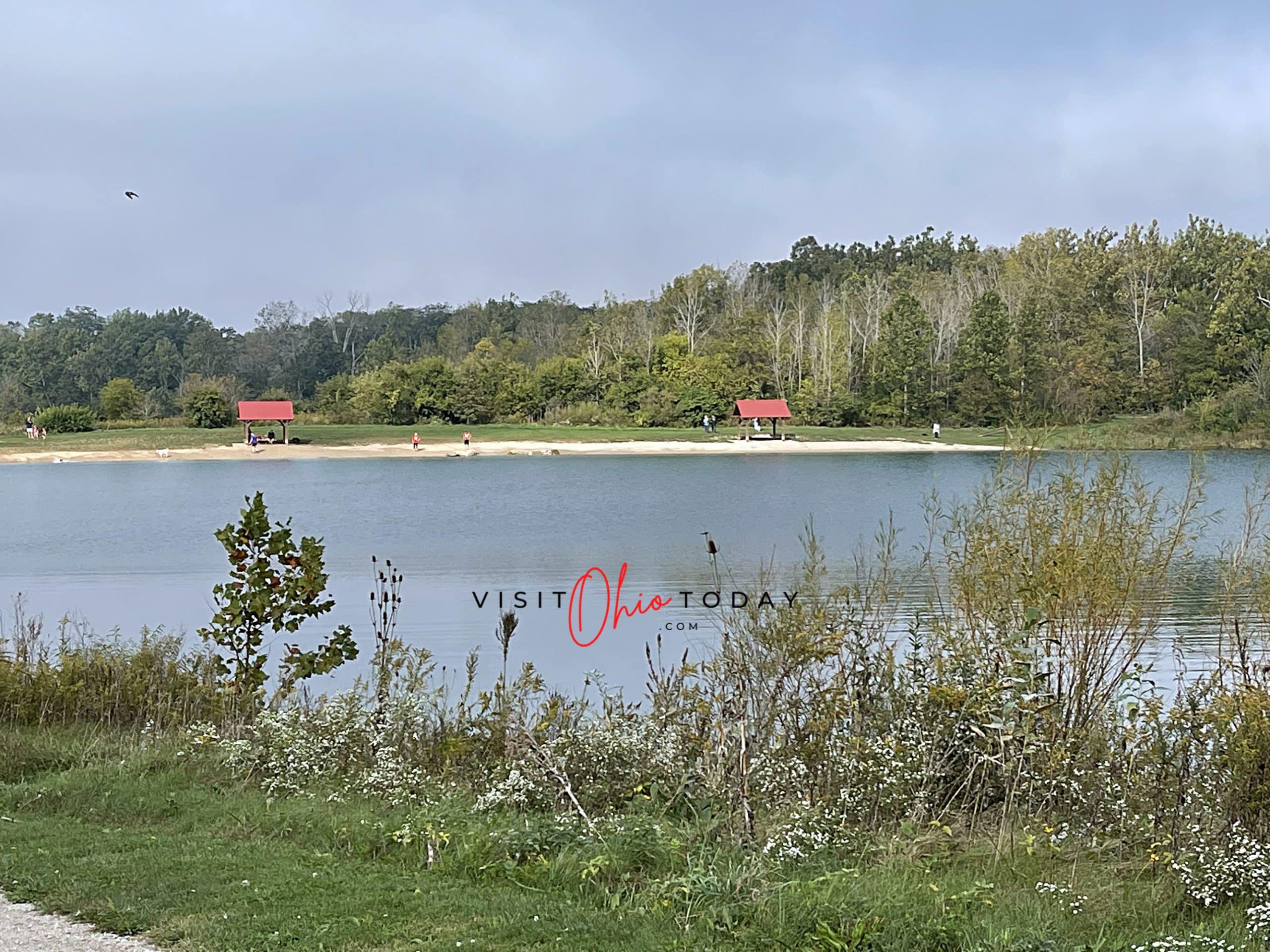 horizontal image of a lake at prairie oaks metro park with shelters in the background and foliage in the foreground