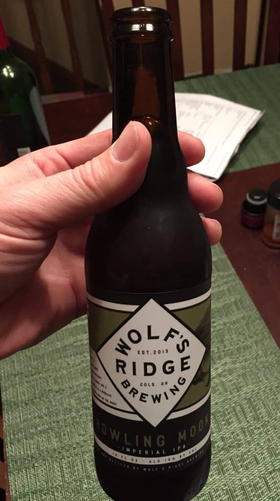 vertical photo showing a hand holding a bottle of wolf's ridge brewing company howling moon imperial IPA