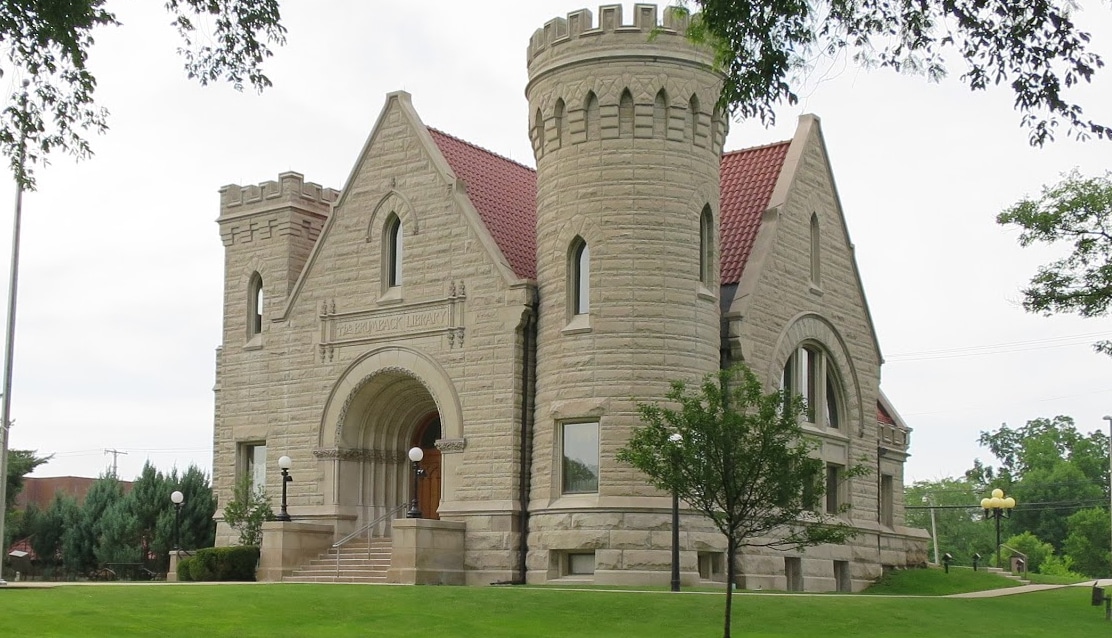 horizontal photo of The Brumback Library with a green lawn in the foreground and tree branches around the edges. For Castles in Ohio. Image via Wikimedia https://commons.wikimedia.org/wiki/File:Brumback_Library_c._1901_-_panoramio.jpg