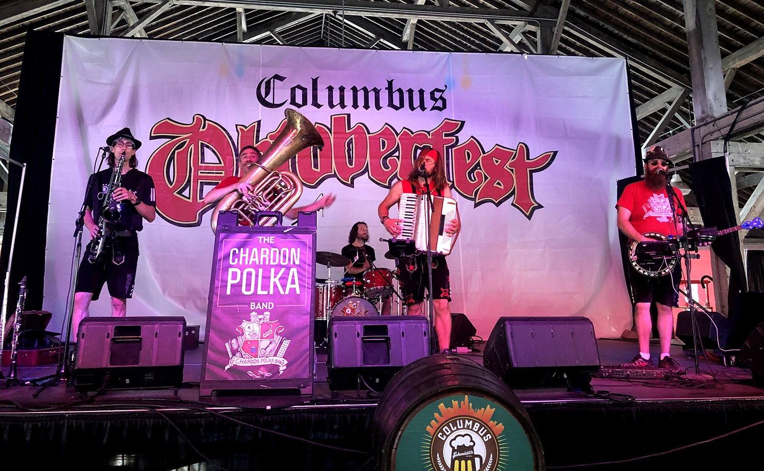 horizontal photo of the Chardon Polka Band on stage at the Columbus Oktoberfest with a large flag backdrop with Columbus Oktoberfest on it. Image: Wikimedia Commons https://commons.wikimedia.org/wiki/File:Chardon_Polka_Band_-_Columbus_Oktoberfest.jpg