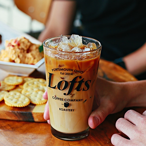 square photo of a frappe in a tall glass with the Lofts logo with some snacks in the background. Image courtesy of Lofts Coffee Company and Roastery