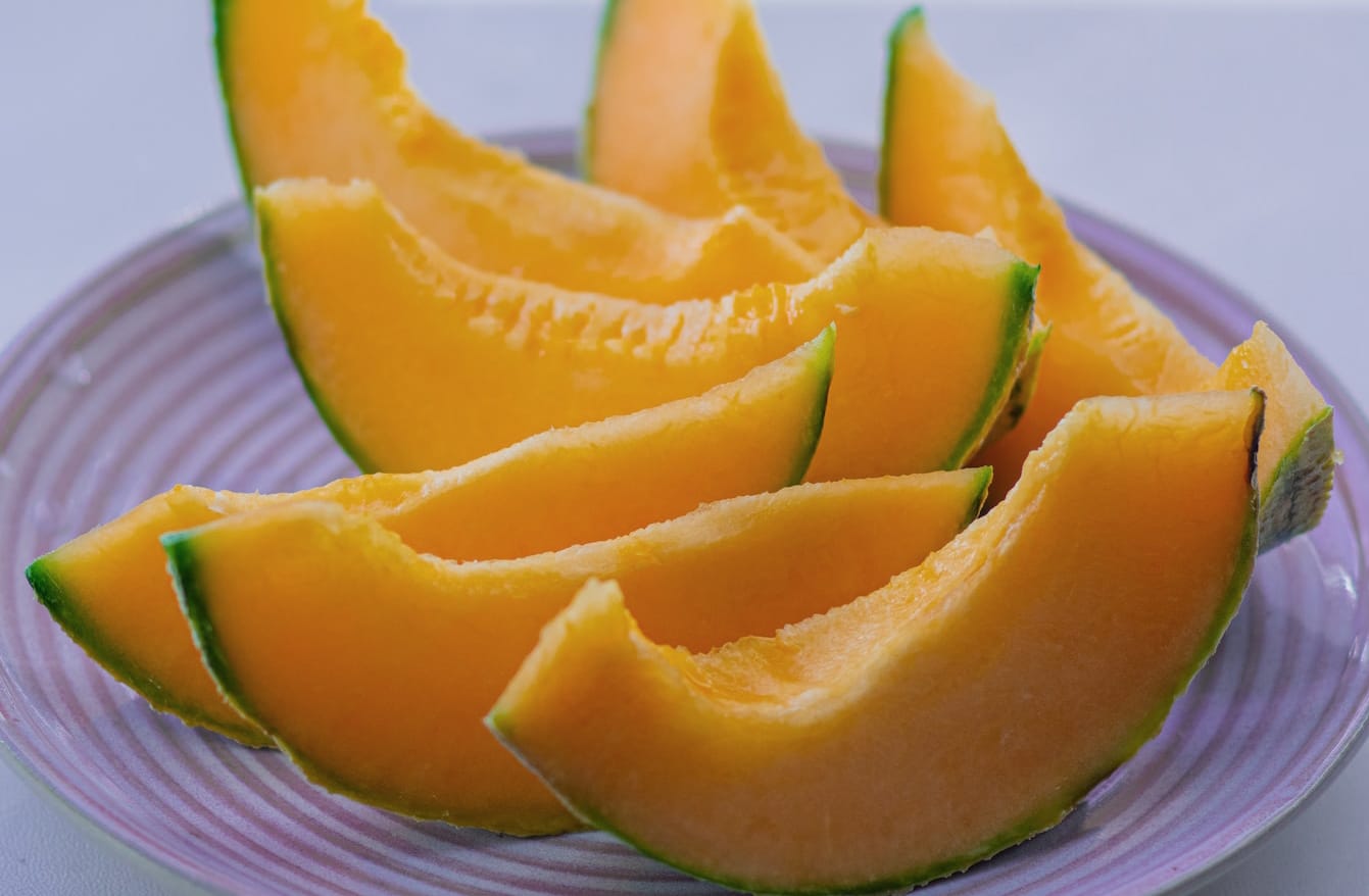 horizontal photo of cantaloupe melon slices on a lilac colored plate. 