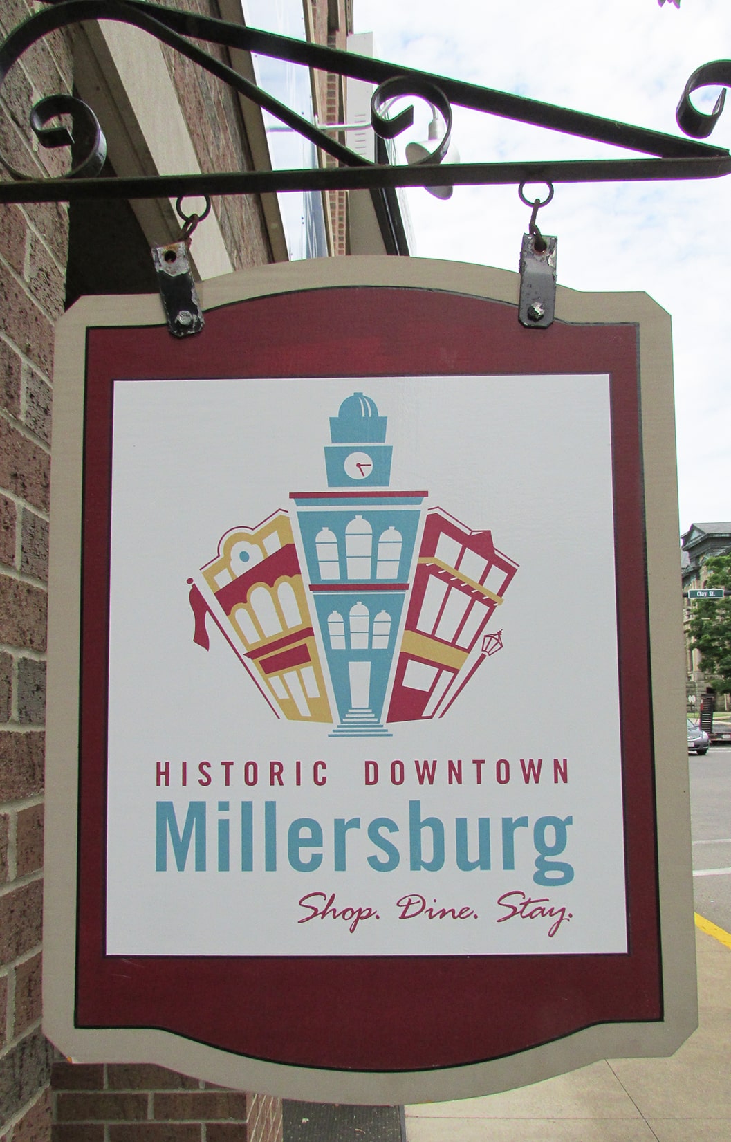 vertical photo showing the Historic Downtown Millersburg sign hanging from a fancy bracket on a wall. Image Wikimedia Commons https://commons.wikimedia.org/wiki/File:6_W_Jackson_2016-06-17_066.jpg