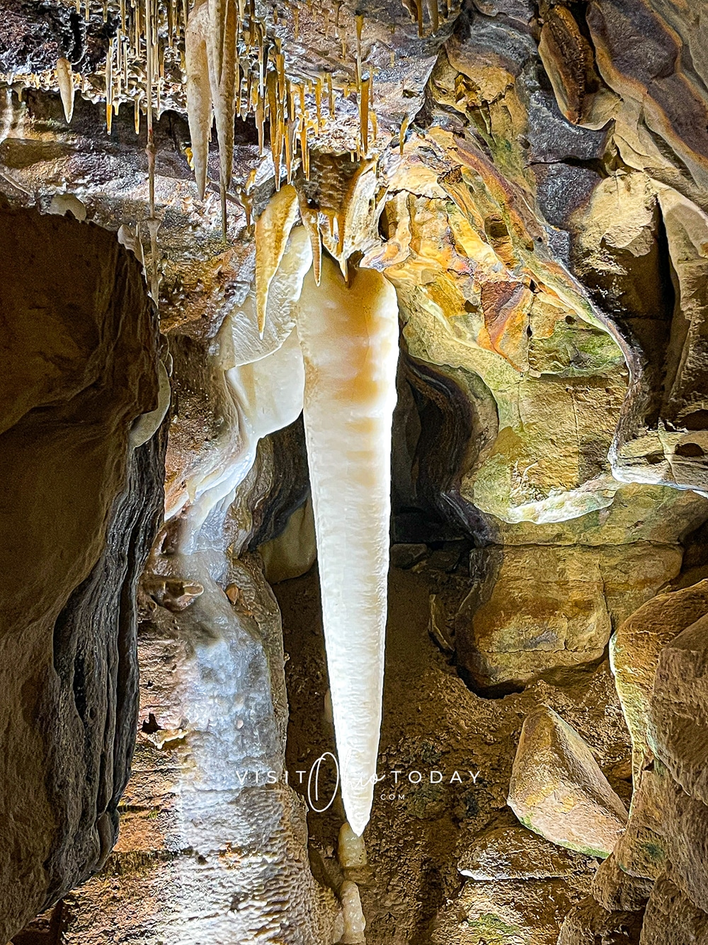 vertical photo of the ohio caverns with a large white stalactite and other small stalactite hanging from the top