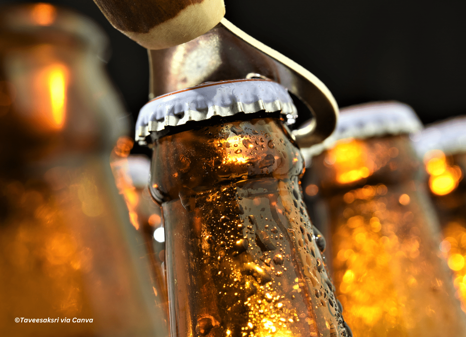 horizontal photo of the cap of a beer bottle being removed with other beer bottles around it