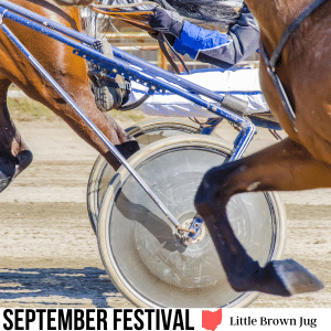 square image with a photo of a close up of a harness race, showing the wheels of a harness and the legs of a couple of horses. A white strip at the bottom has the text September Festival Little Brown Jug. Image via Canva pro license