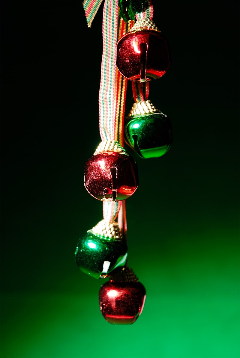 Green background with red and green metal jingle bells hanging on ribbon