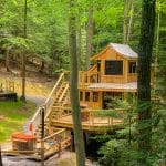 square photo of one of the Hocking Hills Treehouse Cabins, nestled in lots of trees , with stairs up to the cabin.