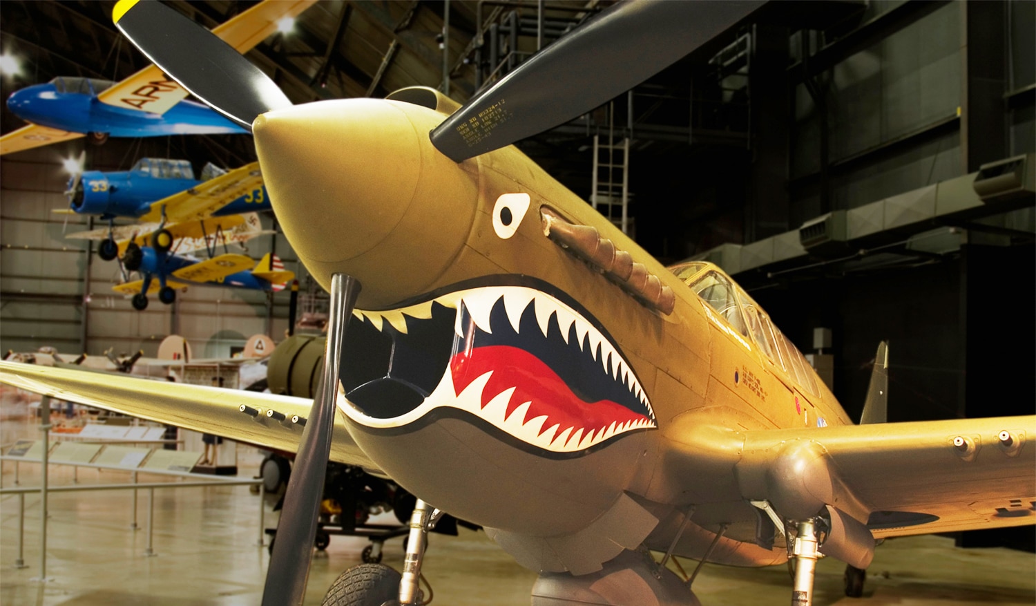 horizontal photo of a yellow airplane with a painted on shark mouth at the National Museum of the US Air Force. Image via Canva pro license